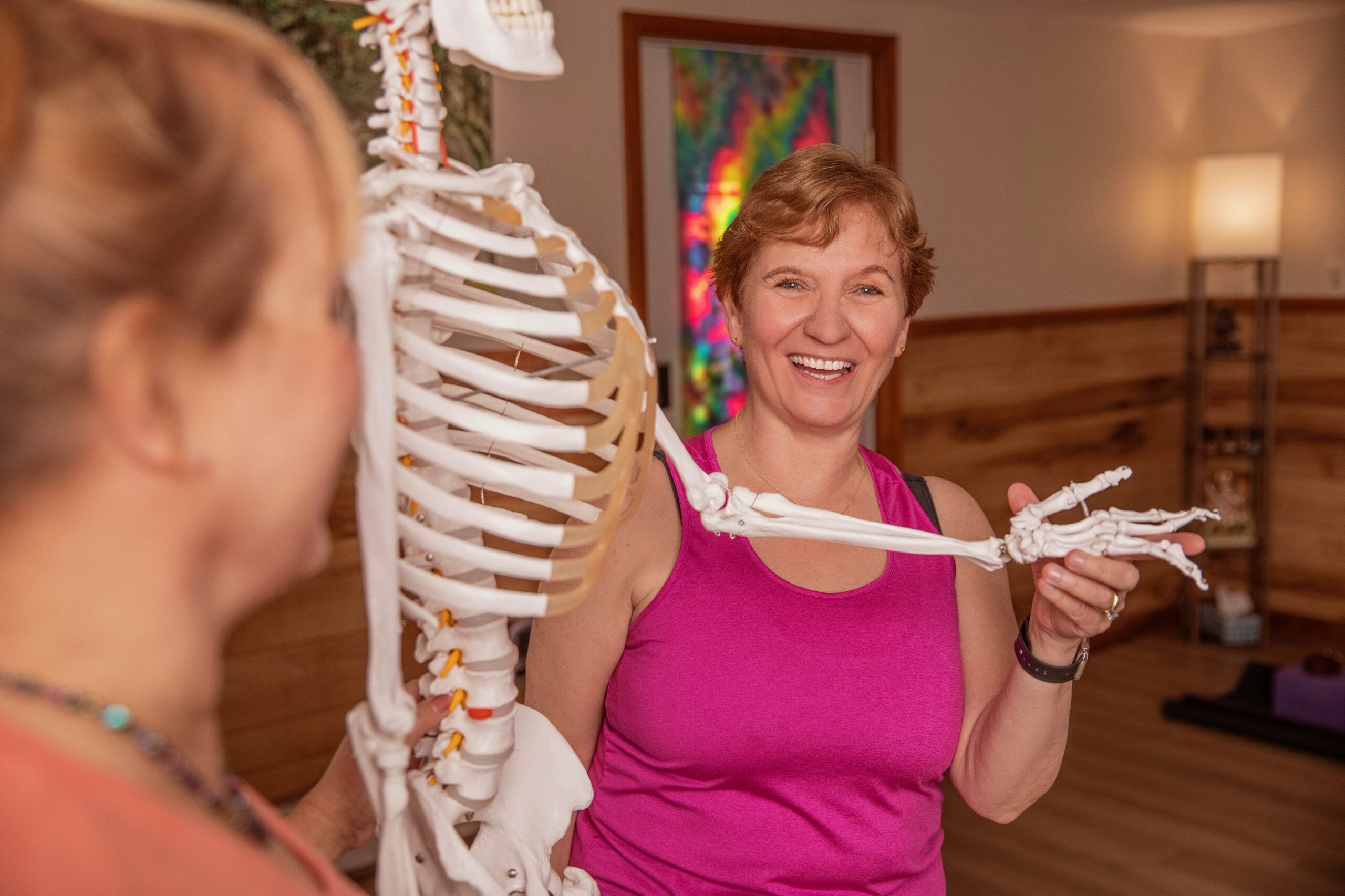 Woman in pink demonstrating with a skeleton model in a classroom.
