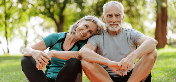 Elderly couple smiling and relaxing outdoors on a sunny day.