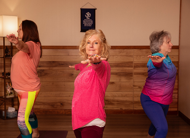 Three women practicing yoga in a studio, each striking a warrior pose.